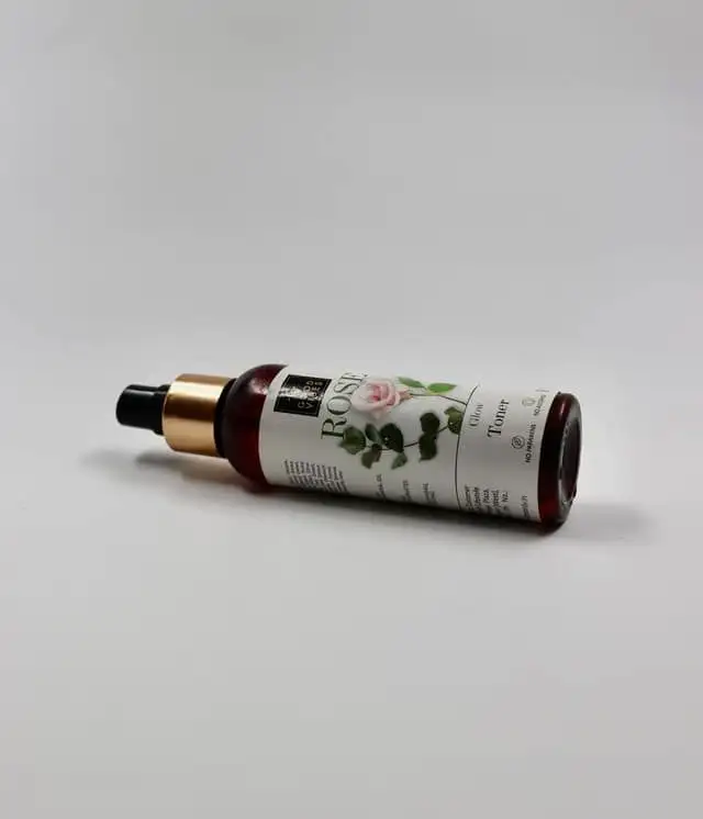 A small cosmetic bottle with a rose-colored label, photographed on a plain white background
